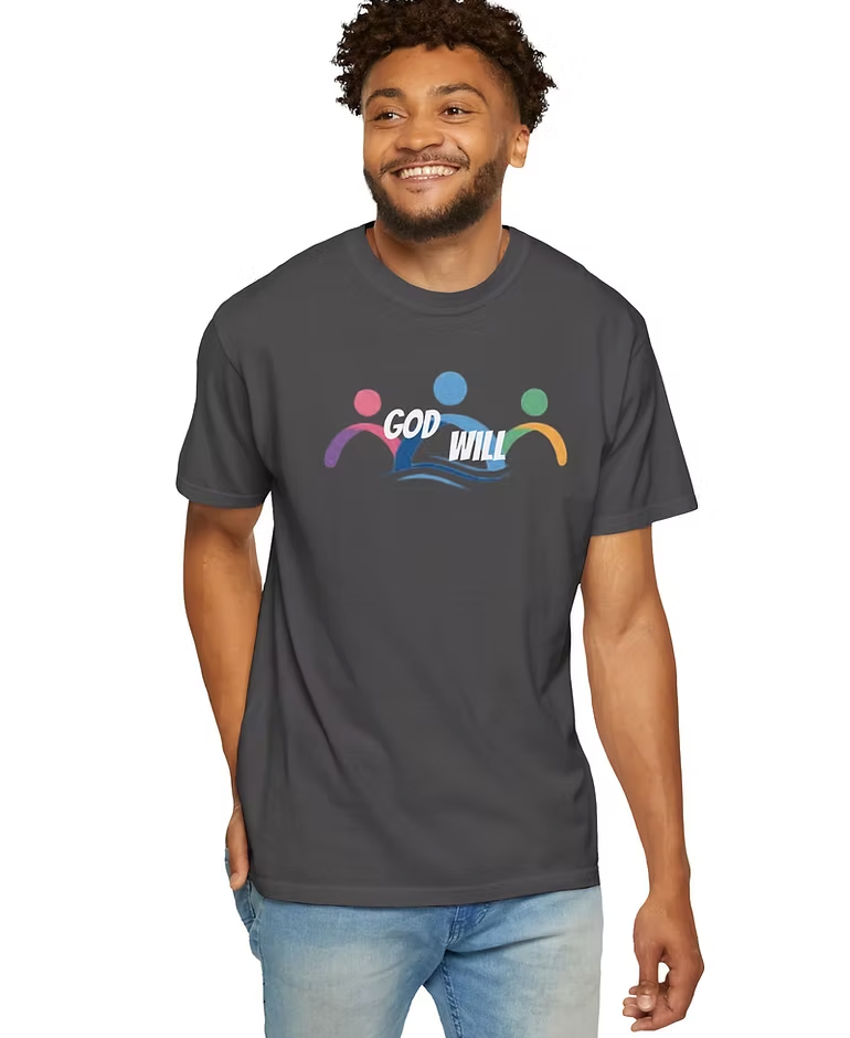 A person wears a dark t-shirt featuring a vibrant graphic design with three stylized human figures in pink, blue, and green arranged in a semi-circle above the phrase “GOD WILL.” The word “GOD” is outlined in pink, while “WILL” is outlined in blue, with a wave-like underline beneath it. The design radiates spiritual affirmation and movement, suggesting divine action, hope, and unity.