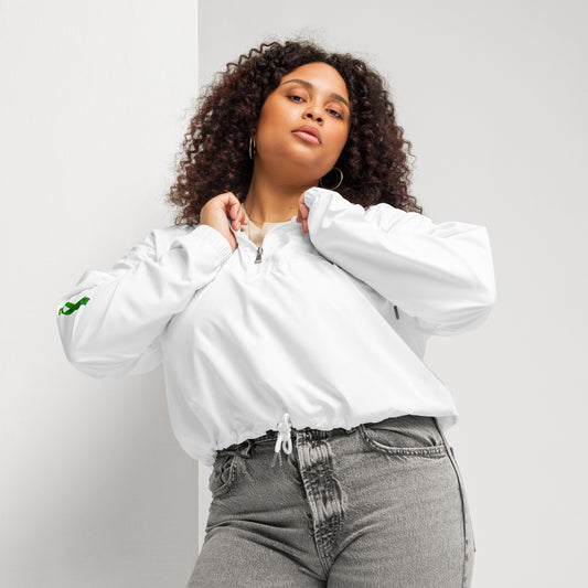 A person poses confidently in a white zip-up pullover with a white zipper and drawstring at the waist, paired with high-waisted gray jeans. The pullover features a small green design on the left sleeve. The individual has curly hair and holds the collar with both hands, standing against a plain background. The outfit blends casual comfort with modern style, subtly hinting at advocacy through the green sleeve detail.