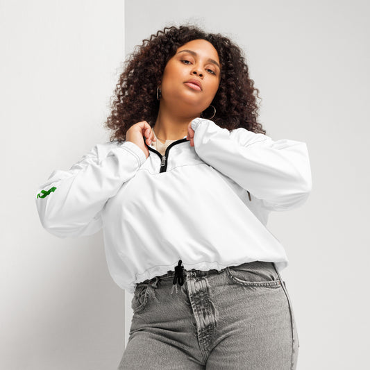 A person poses confidently in a white zip-up pullover with a black zipper and drawstring at the waist, paired with high-waisted gray jeans. The pullover features a small green design on the left sleeve. The individual has curly hair and holds the collar with both hands, standing against a plain background. The outfit blends casual comfort with modern style, subtly hinting at advocacy through the green sleeve detail.