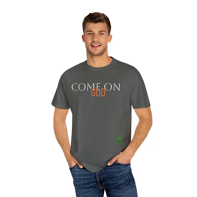 A man wears a dark gray t-shirt with the phrase “COME ON GOD” printed on the front. The words “COME ON” are in bold white uppercase letters, while “GOD” stands out in bright orange. A small green awareness ribbon is placed near the bottom right of the shirt. The design conveys a spiritual or motivational message, possibly expressing a plea for strength or guidance, while the ribbon suggests advocacy for mental health or related causes.