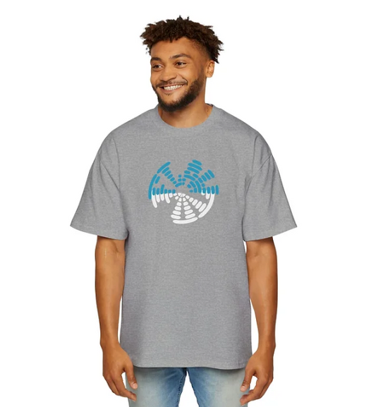 A person wears a gray t-shirt with a circular graphic design on the front composed of segmented blue and white shapes arranged to suggest motion or rotation. The person stands smiling with relaxed posture, hands at their sides. The design evokes themes of energy, rhythm, and quiet impact—ideal for campaigns centered on emotional resonance, frequency, or inner strength.