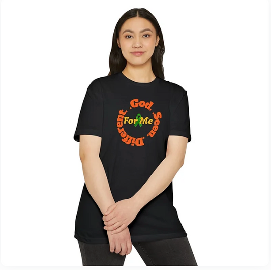 A person wears a black t-shirt featuring the phrase “God Sees Different For Me” arranged in a circular layout around a green and orange graphic element. The design blends faith-based affirmation with vibrant color, suggesting divine perspective and personal uniqueness. The person stands confidently, embodying the shirt’s message of spiritual identity and intentional vision.
