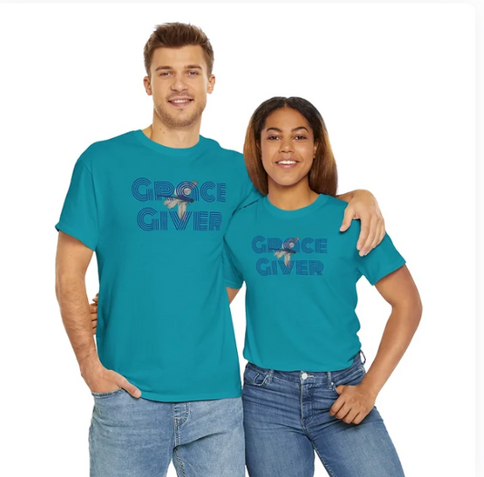 Two individuals stand side by side, smiling and wearing matching turquoise t-shirts with the phrase “GRACE GIVER” printed in bold dark blue letters. A stylized heart with a cross at its center is integrated between the words, reinforcing the shirt’s faith-based message. Their arms are around each other, radiating warmth, unity, and spiritual encouragement. The design celebrates compassion, divine grace, and the power of shared belief.