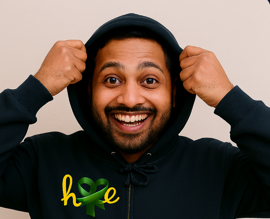 A person smiles broadly while holding the hood of a black hoodie with both hands. The front of the hoodie features the word “hope” in lowercase white letters, with the “o” replaced by a green awareness ribbon. The design blends simplicity with emotional impact, offering a message of resilience, advocacy, and quiet strength.