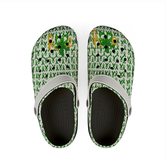 A pair of white clogs are covered in a pattern of green awareness ribbons. Each clog features a cheerful green character with a mustache and hat, resembling a leprechaun, alongside the word “HOPE” in bold yellow and green letters. The interior is black with a textured footbed. The design blends playful charm with advocacy, offering a whimsical yet powerful message of support and visibility.