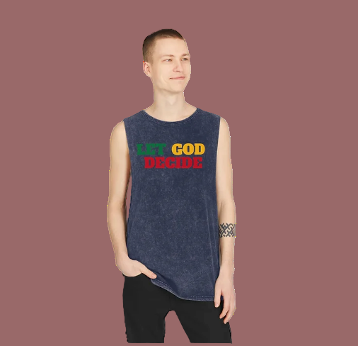 A person stands with one hand in their pocket, wearing a sleeveless black acid-washed shirt that reads "LET GOD DECIDE." The phrase is split into three colors: "LET" in green, "GOD" in yellow, and "DECIDE" in red. The individual has a short haircut and displays a patterned armband tattoo on their left arm. The minimalist background keeps the focus on the shirt’s bold design, which blends spiritual messaging with edgy streetwear style.