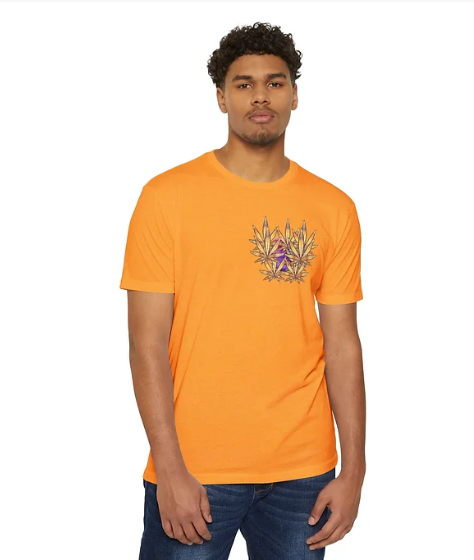 A person stands against a plain white background wearing an orange T-shirt with a vibrant graphic design on the chest. The artwork features a symmetrical arrangement of geometric shapes and leaf-like elements in green and yellow, centered around a bold purple star-like figure. The person pairs the shirt with dark blue jeans, creating a clean and visually engaging look that highlights the shirt’s colorful and artistic design.