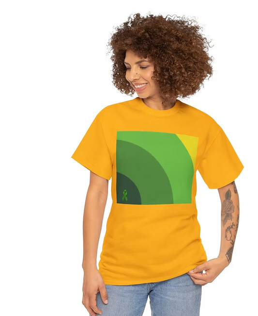 A person stands casually with one hand on their hip, wearing a bright orange T-shirt featuring a bold green graphic. The design consists of overlapping arc-like shapes in varying shades of green, creating a layered, concentric pattern. A small green ribbon symbol is placed in the bottom left corner of the graphic. The contrast between the orange shirt and green design makes the artwork visually striking, while the ribbon may suggest support or awareness for a cause. The person is smiling and looking slightl