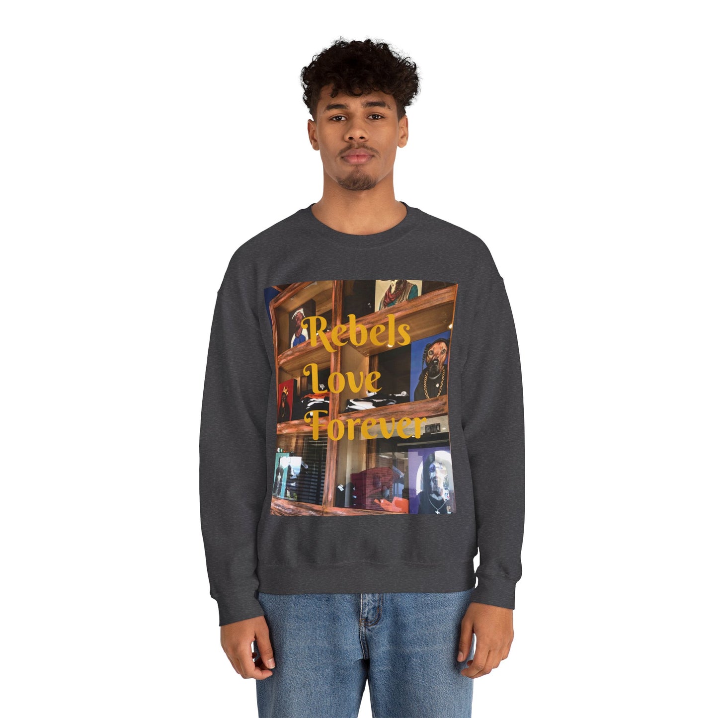 A person wears a dark-colored sweatshirt featuring a vibrant collage-style graphic on the front. The design blends warm-toned urban and indoor scenes with overlaid yellow text that reads "Rebels Love Forever." The imagery evokes a sense of intimacy and rebellion, combining photographic art with expressive typography to create a visually rich and emotionally resonant fashion statement.