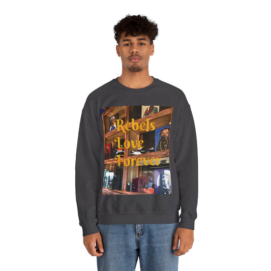 A person wears a dark-colored sweatshirt featuring a vibrant collage-style graphic on the front. The design blends warm-toned urban and indoor scenes with overlaid yellow text that reads "Rebels Love Forever." The imagery evokes a sense of intimacy and rebellion, combining photographic art with expressive typography to create a visually rich and emotionally resonant fashion statement.