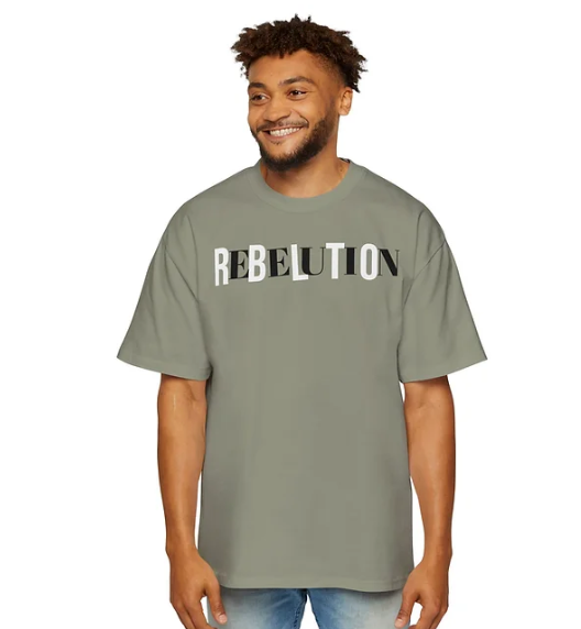 A person stands smiling in a loose-fitting olive green T-shirt with the word "REBELLION" printed boldly across the chest. The capital letters alternate between black and white vertical segments, creating a visually striking and high-contrast effect. Set against a plain white background, the shirt’s graphic design takes center stage, offering a bold statement piece that channels streetwear energy and themes of defiance and individuality.