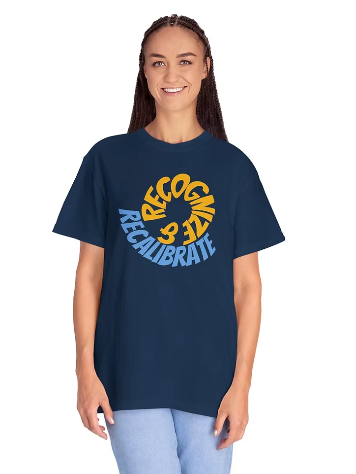 A person wears a navy blue T-shirt featuring a circular graphic on the front. The design displays the words "RECOGNIZE" in yellow and "RECALIBRATE" in blue, arranged in a spiral loop that transitions seamlessly from one word to the other. This cyclical layout visually reinforces the message of awareness and adjustment, making the shirt a compelling piece for those drawn to themes of mindfulness, growth, and intentional change.