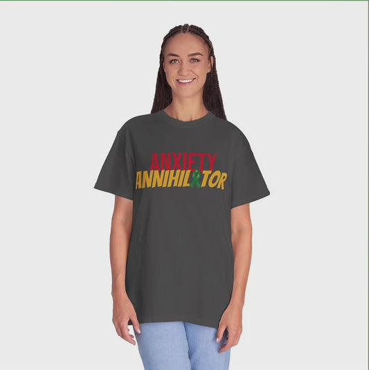 A person stands smiling in casual attire, wearing a black t-shirt with bold, colorful lettering that reads “ANXIETY ANNIHILATOR.” The word “ANXIETY” is in red, while “ANNIHILATOR” is in yellow, with a green star replacing the final “A.” They pair the shirt with light blue pants, radiating confidence and positivity. The shirt’s message suggests empowerment and mental health advocacy.